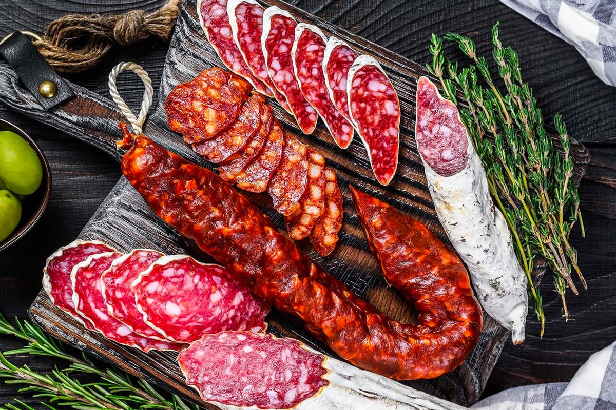 Top view of different types of salami near aromatic herbs.