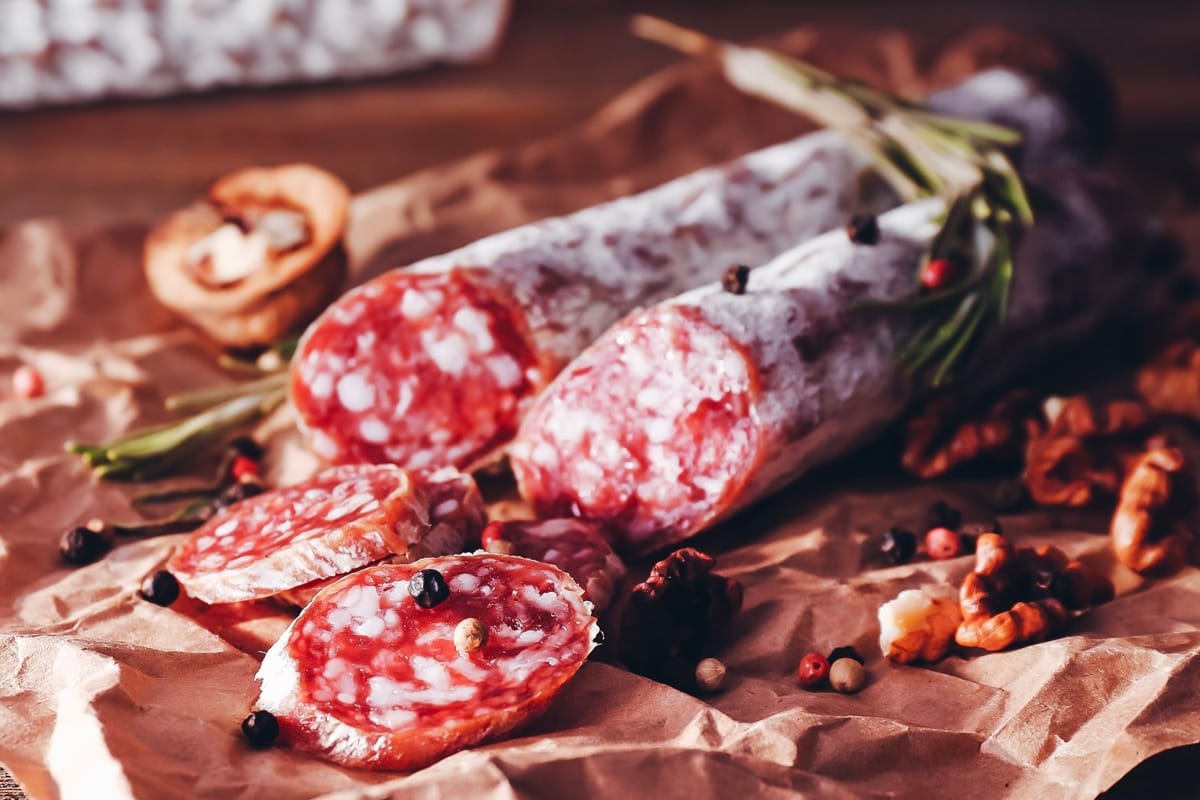 Dried salami near peppercorns, rosemary and nuts.