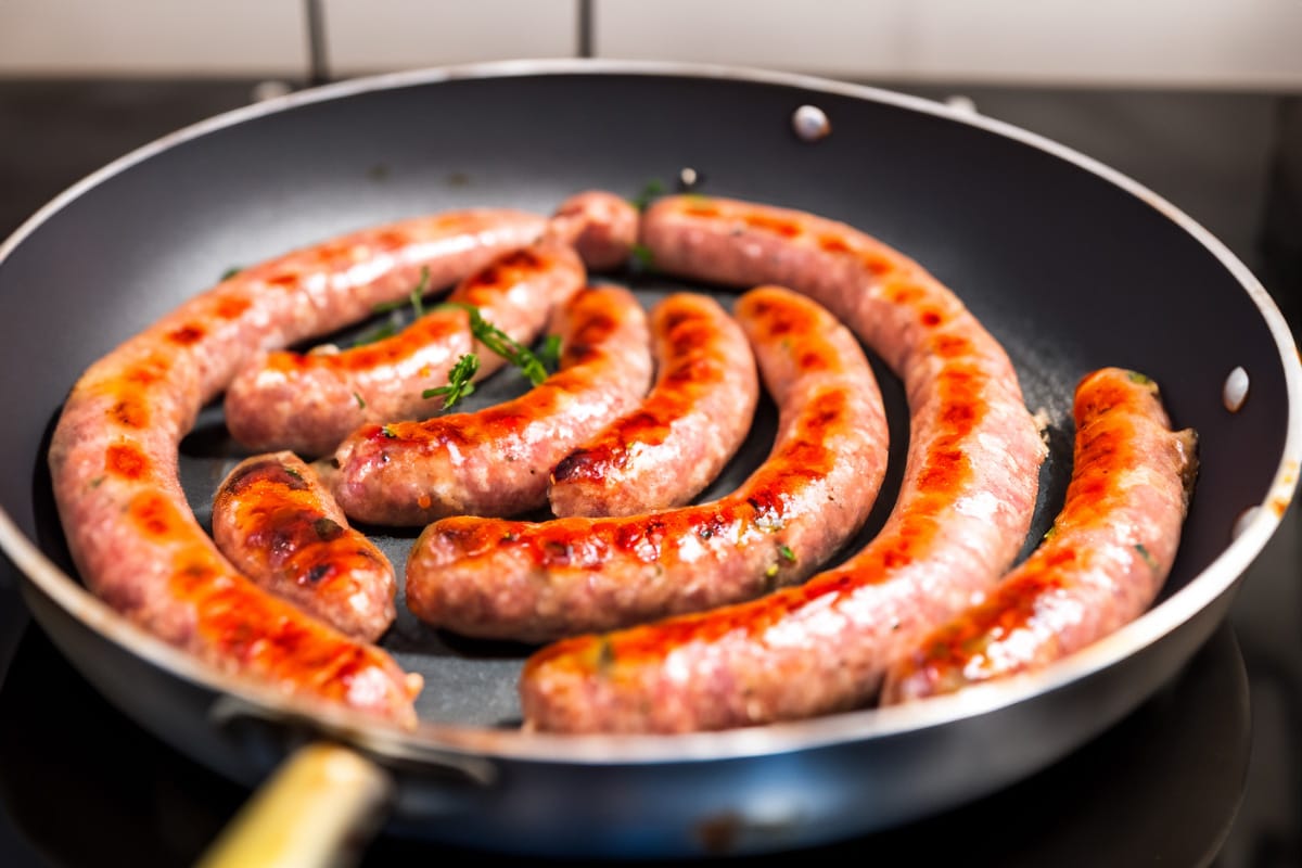 Skillet with cooked sausages on the stove.