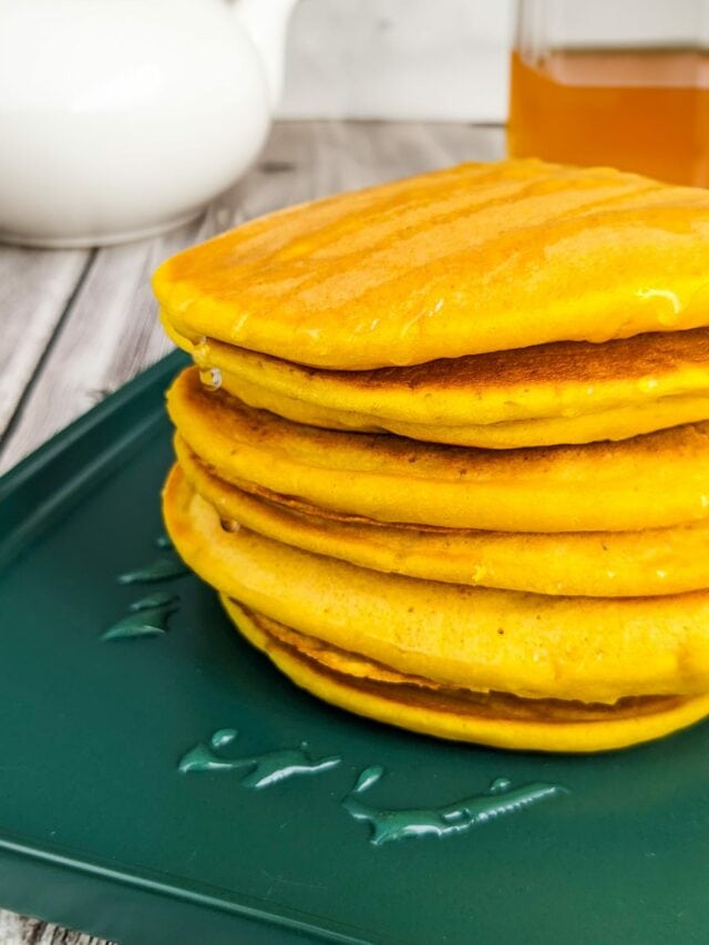 Stuck of fluffy pumpkin pancakes on a green plate near a pot of tea and honey.