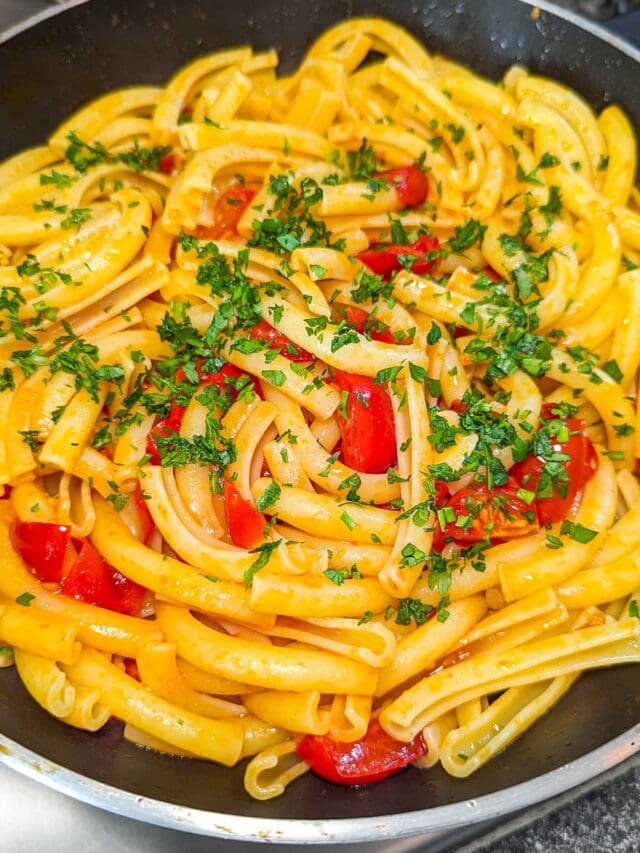 Close look of a pan of pasta with tomatoes, garlic and parsley.
