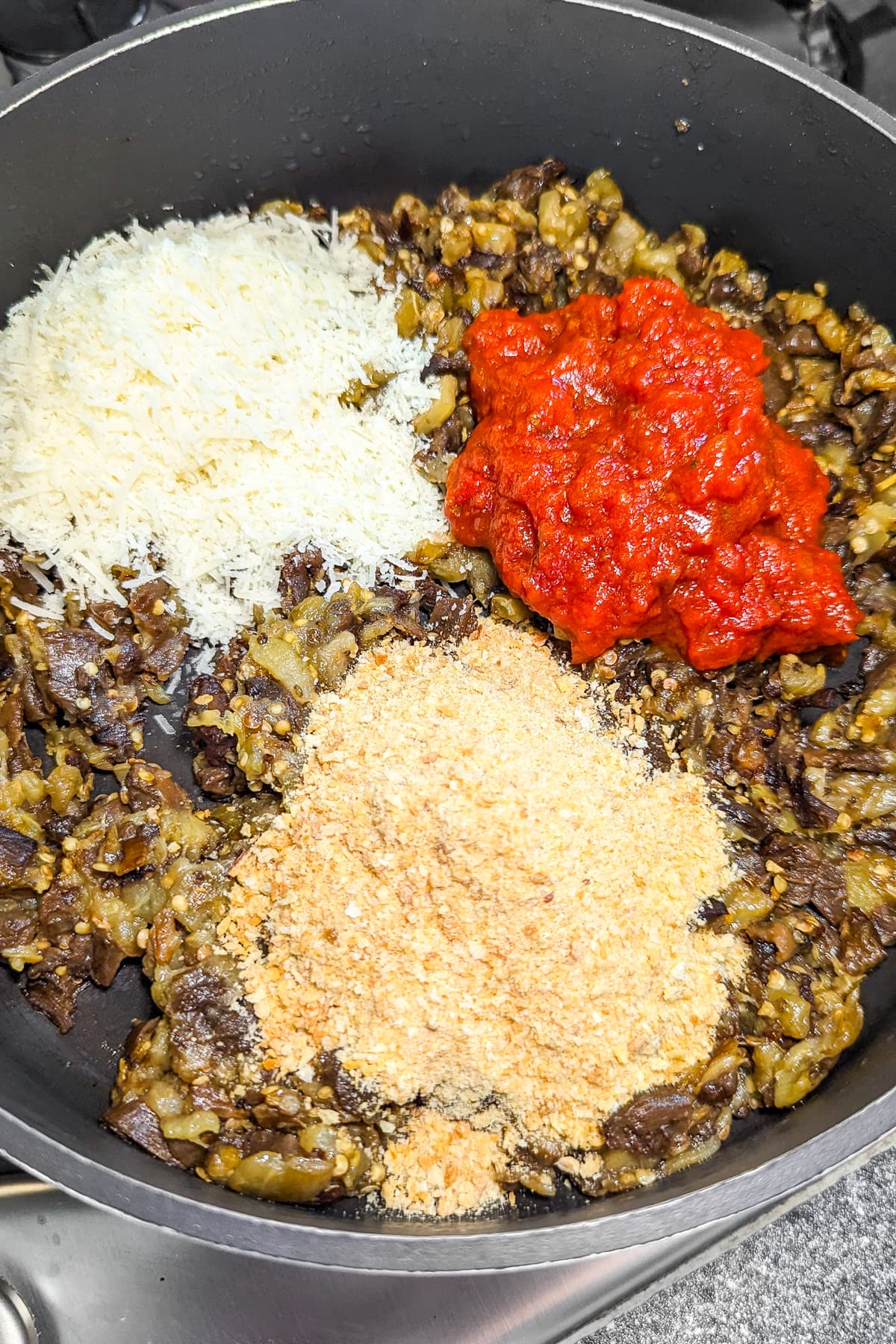 A pan on the stove with a mixture of eggplants, breadcrumbs and tomato sauce.