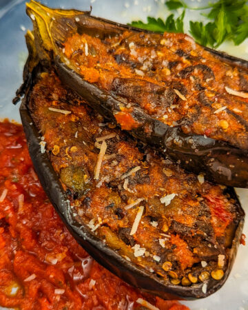 Close look of two eggplant boates with shredded parmesan and marinara sauce near them.