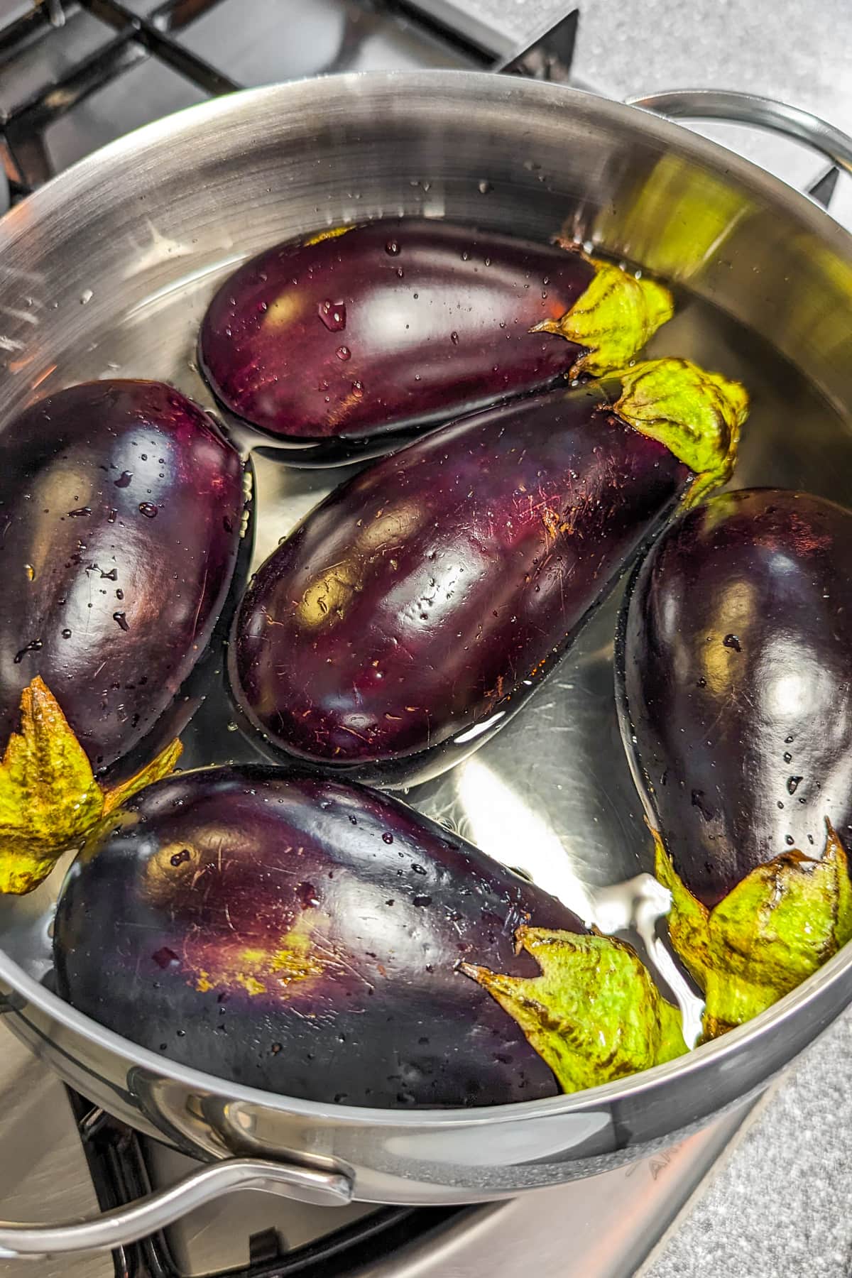 5 small eggplants soaked in water in an aluminum pan on the stove.