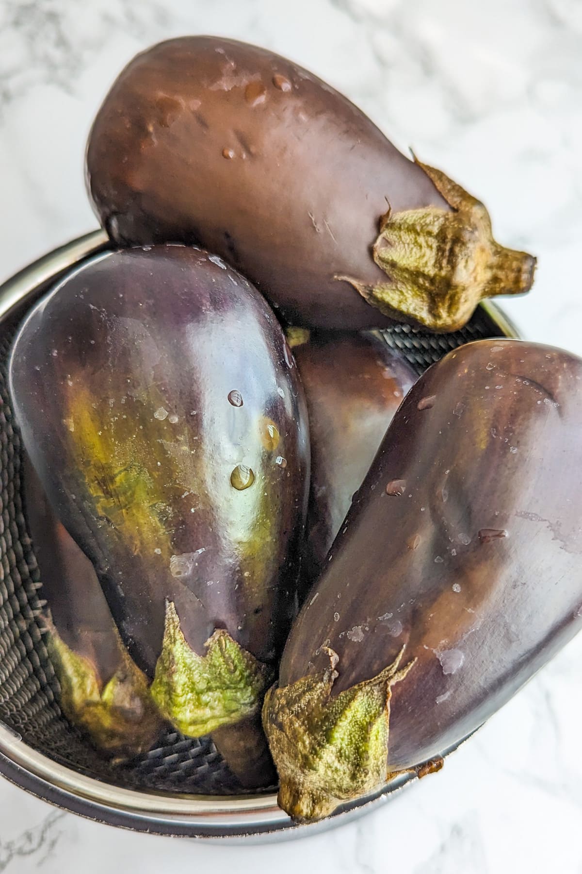 Eggplants sitting on a sieve on a white marble table.