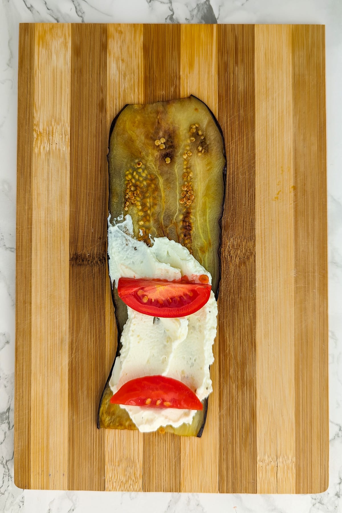 A slice of roasted eggplant spreaded with cream cheese and two tomato slices.
