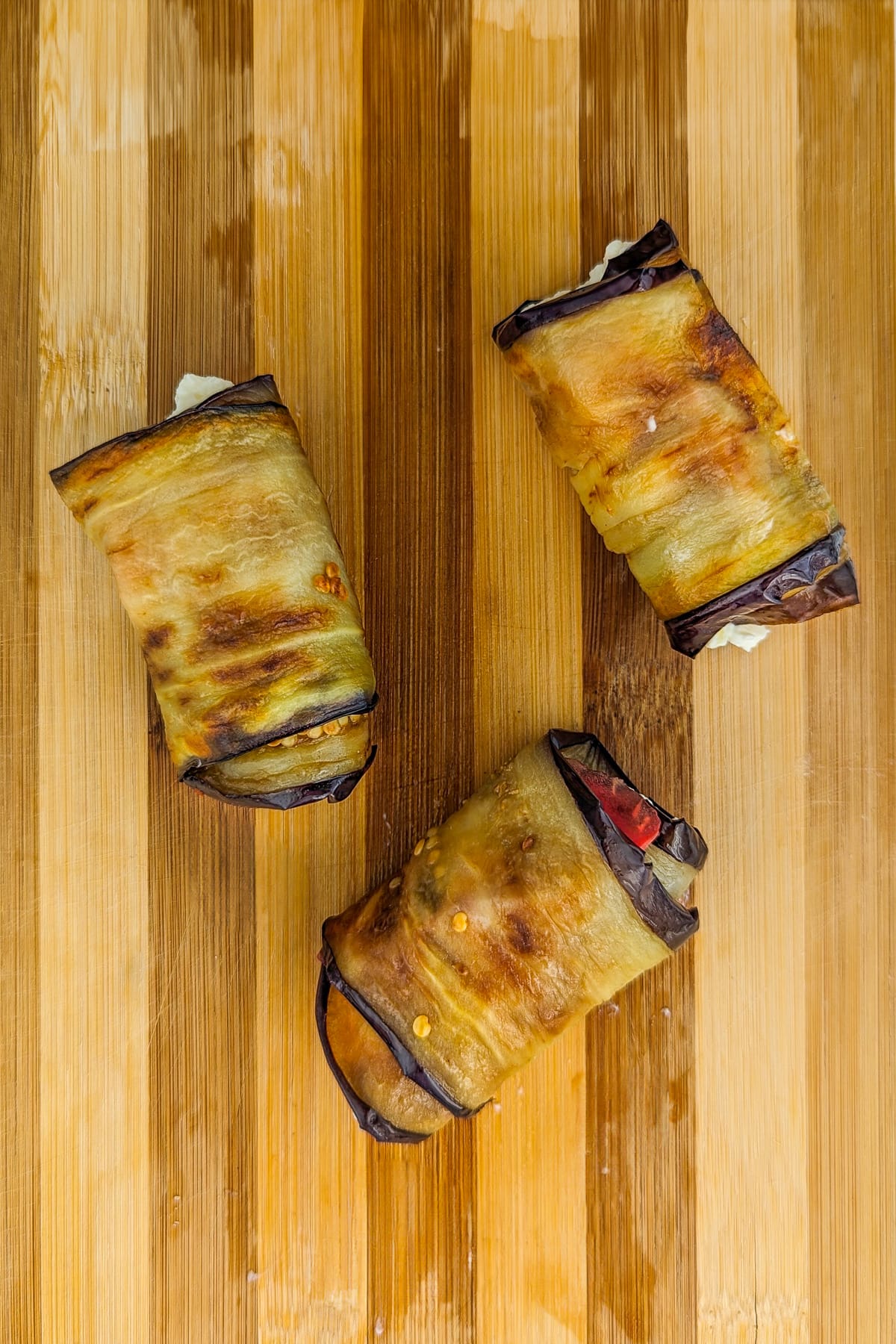 Close view of eggplant and cheese rolls on a wooden cutting board.