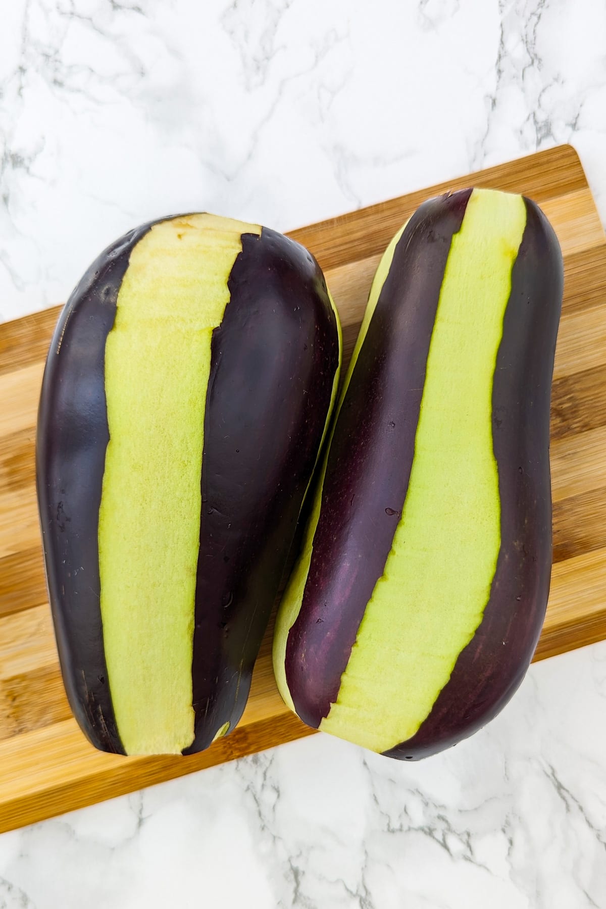 2 large eggplants with lines on them on a cutting board.
