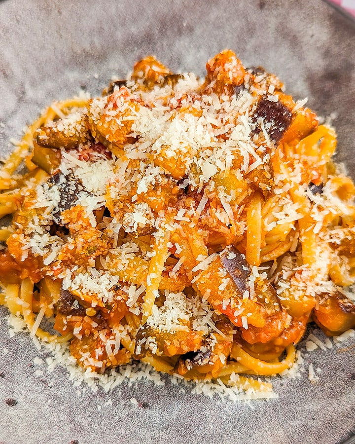 Vintage plate with eggplant pasta and shredded parmesan on a blue wooden table.