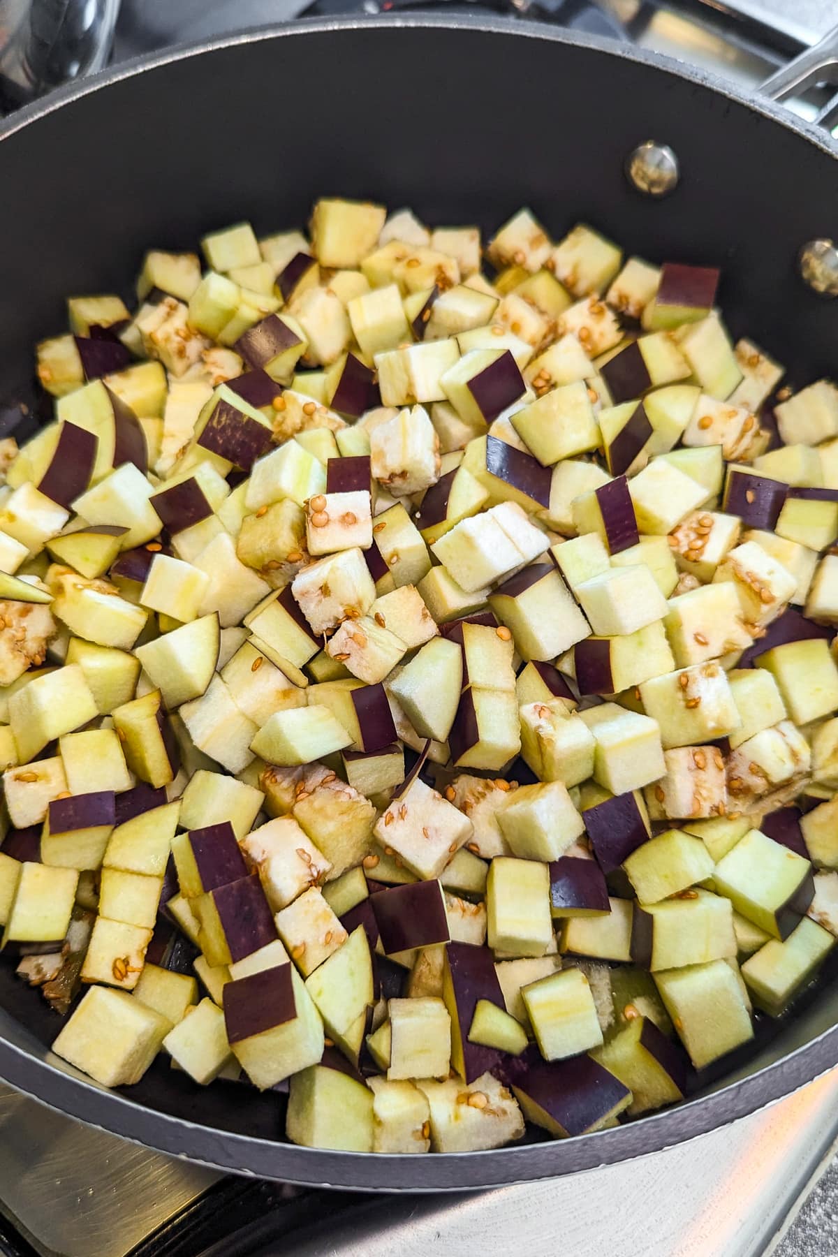 Close look of diced eggplant in a frying pan on the stove.