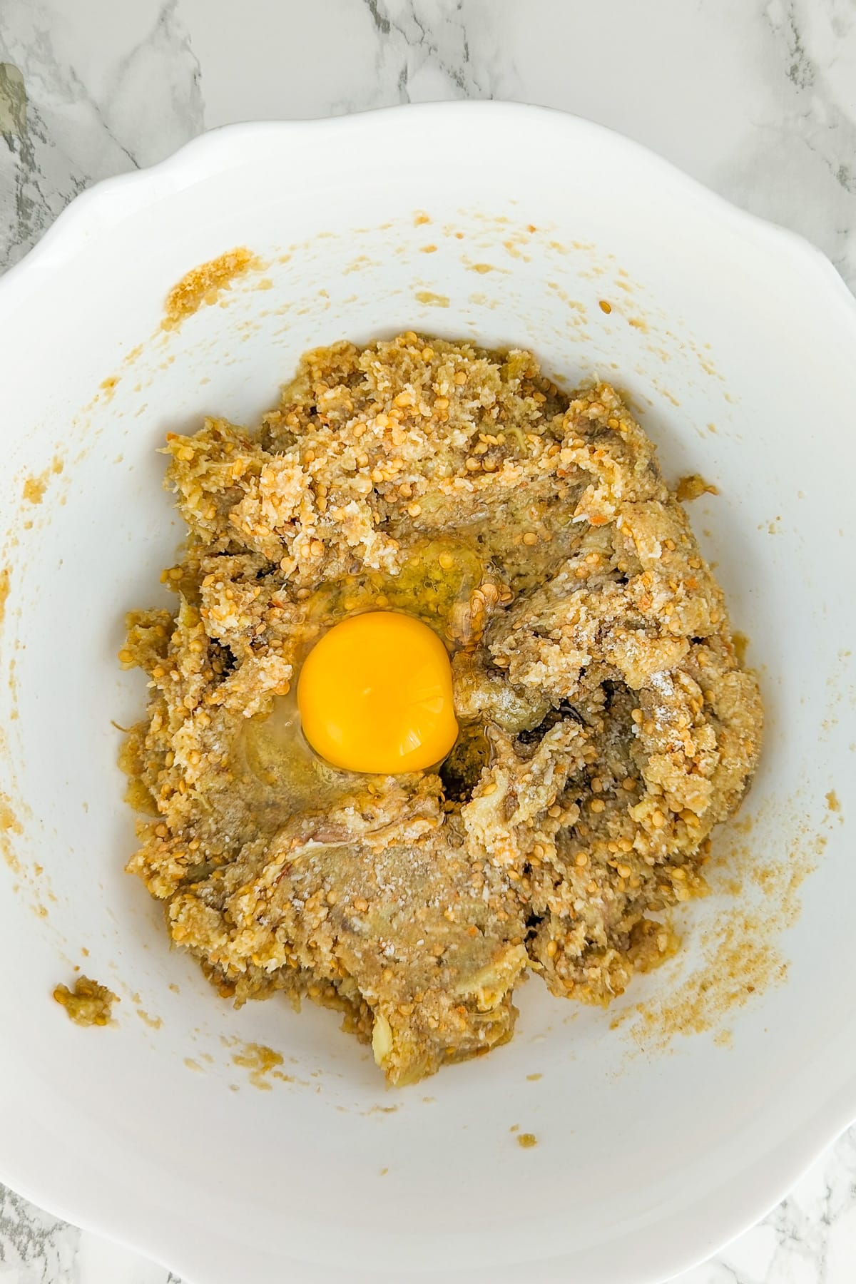 Top view of a white large bowl with eggplant mixture covered with a raw egg.