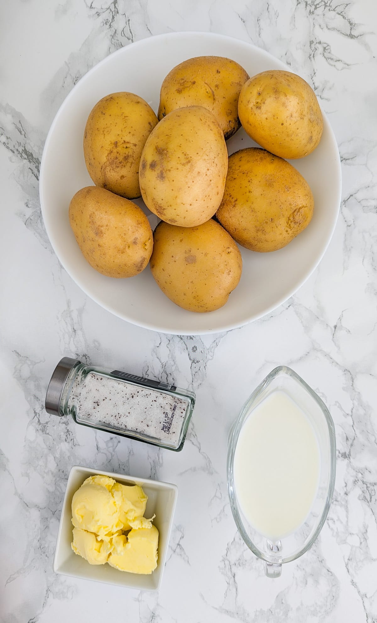Top view of 7 white potatoes on a white plate near butter, and milk.