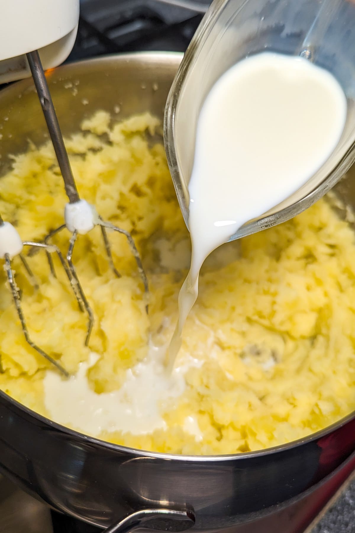 Pouring waster over mashed potatoes in a pan on the stove.