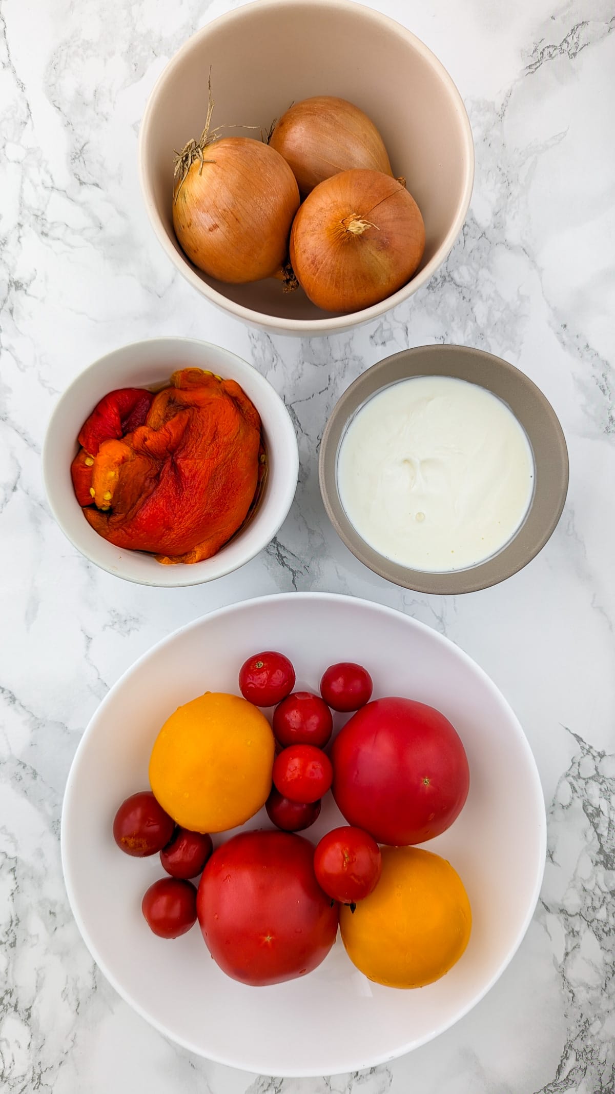 Top view of different tomatoes, roasted bell peppers, cream and onions on a white marble table.