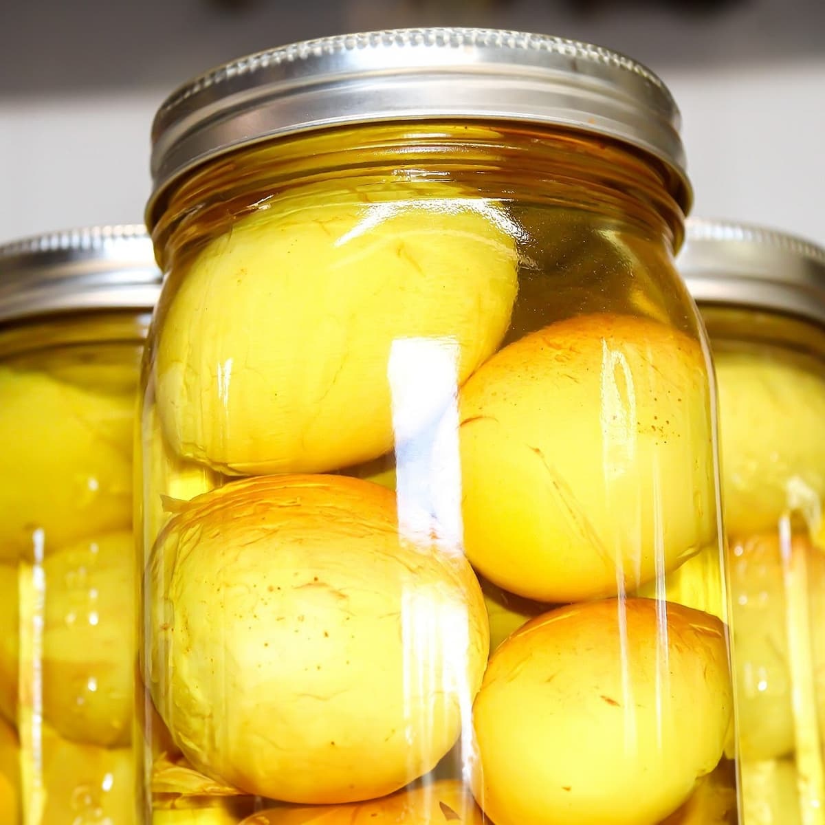 Side view of 3 transparent jars with yellow pickled eggs.