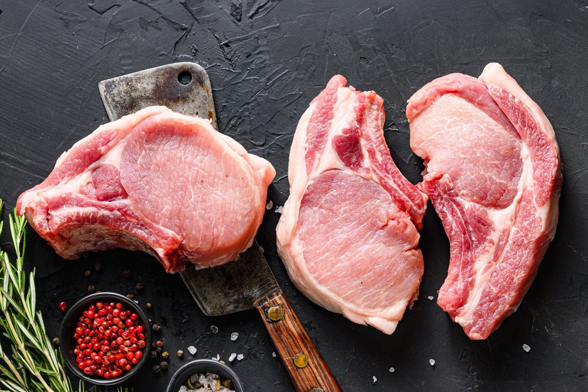 Top view of 3 pieces of pork chops isolated on black background near rosemary and red pepper.