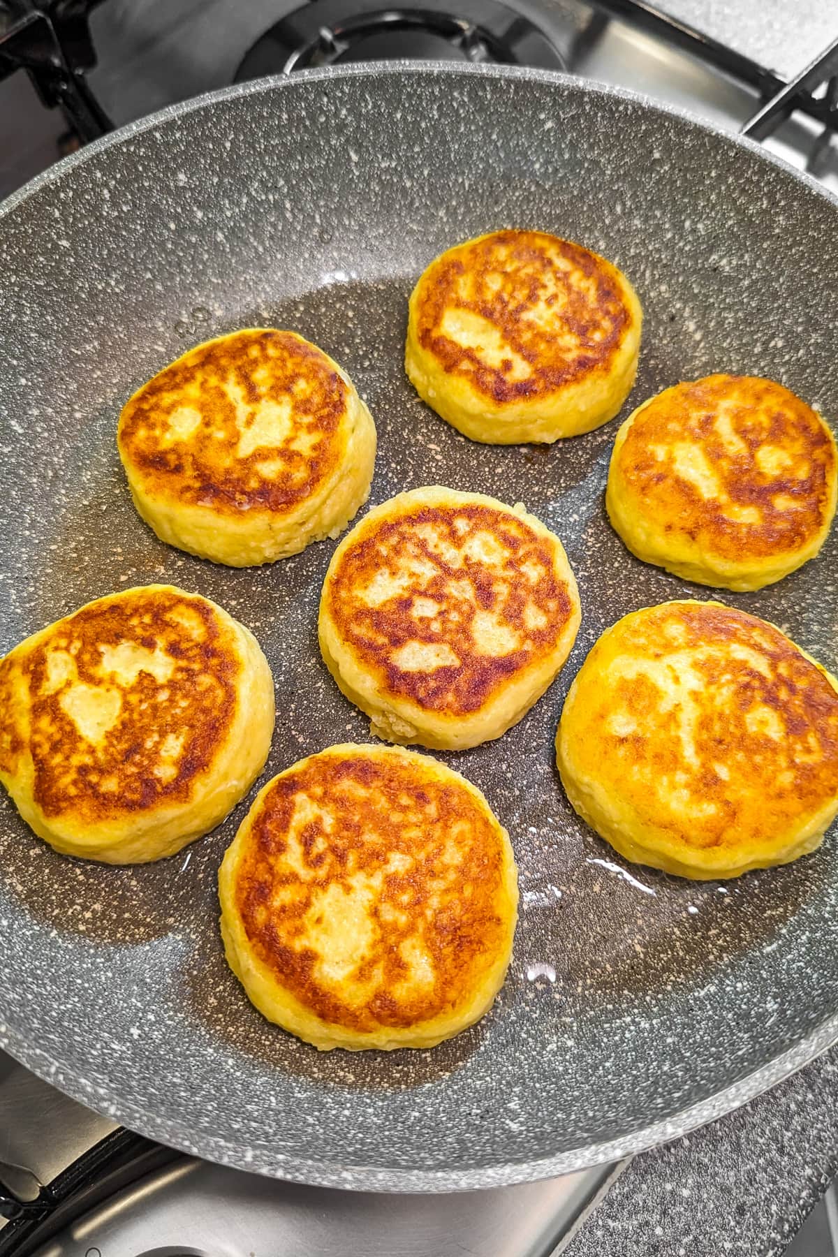 7 fried potato pancakes on frying pan on the stove.
