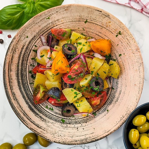 Vintage plate with a salad of potatoes, tomatoes, onions and olives.