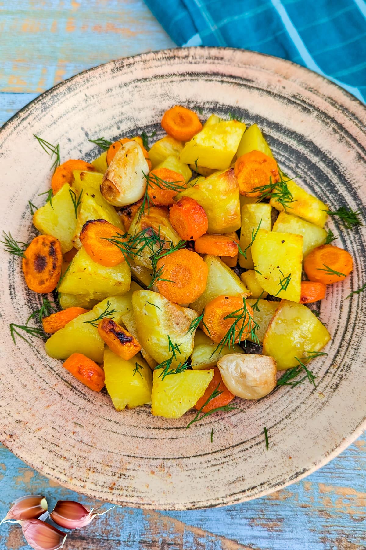 Close view of roasted potatoes, carrots and dill in a vintage plate.