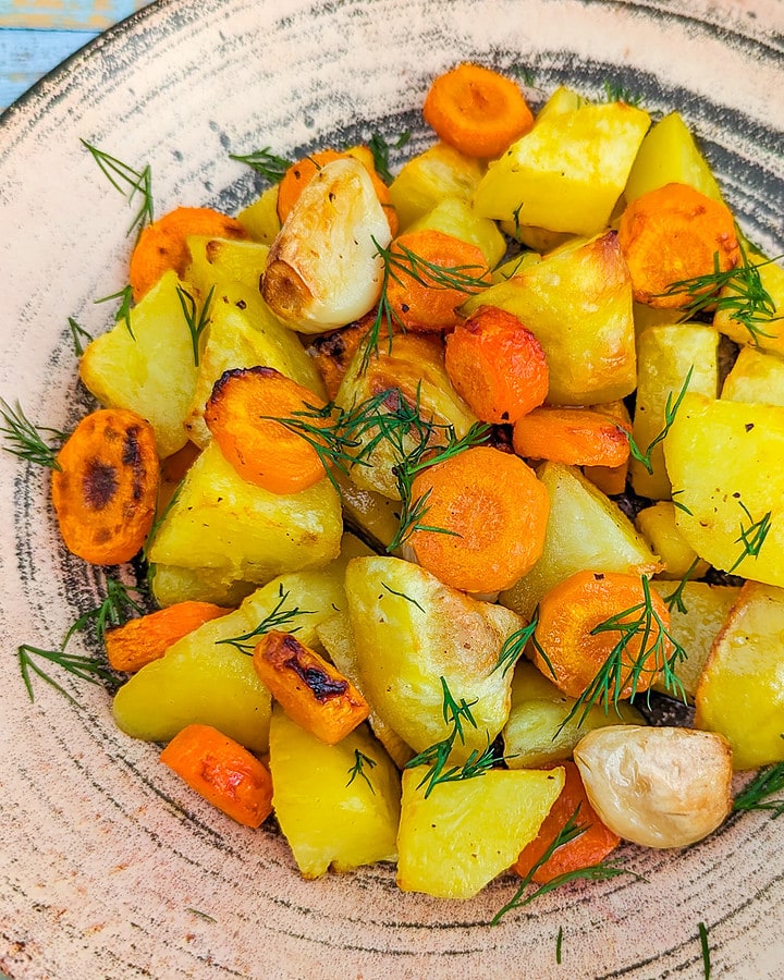 Close view of roasted potatoes, carrots and dill in a vintage plate.