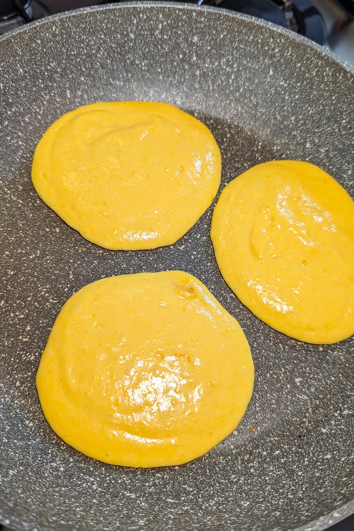 Top view of 3 pumpkin pancakes in a frying pan on the stove.