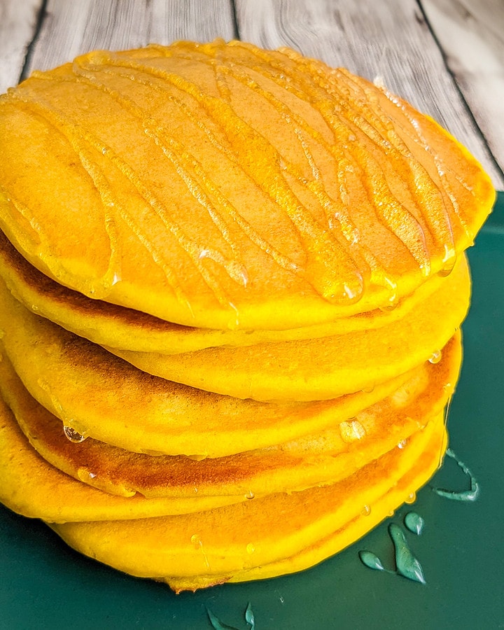 Stuck of fluffy pumpkin pancakes on a green plate near a pot of tea and honey.