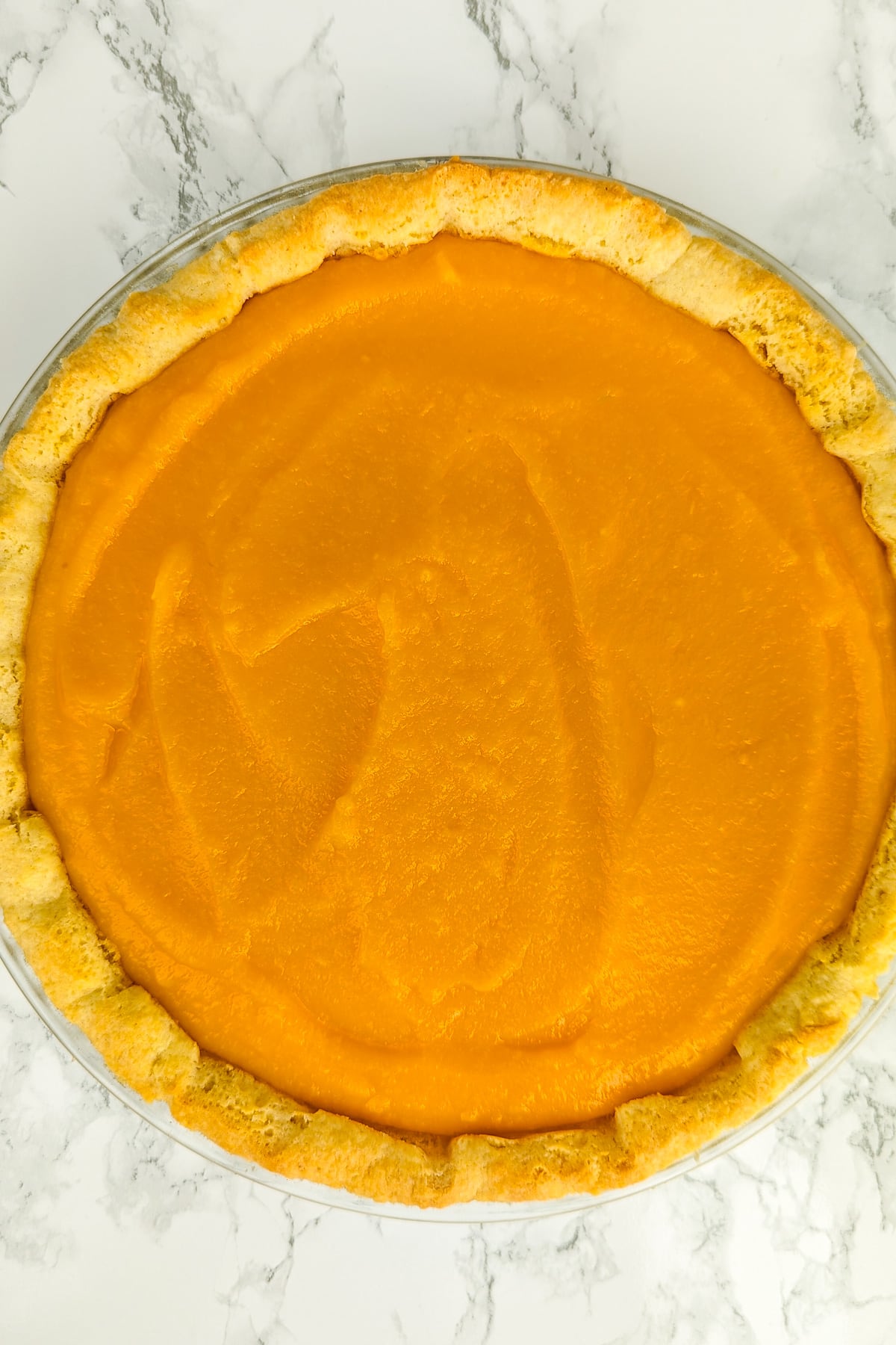 Top view of pumpkin pie on a white marble table.