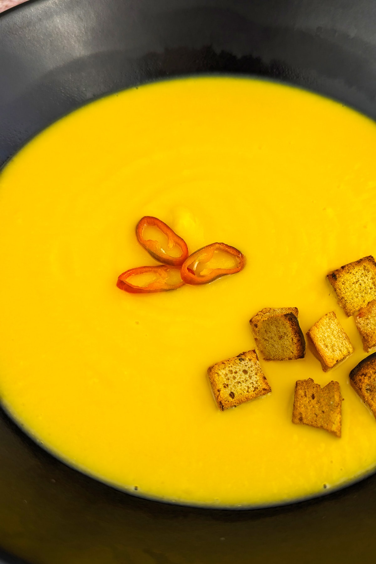 Close look of potato soup with croutons in a black plate.