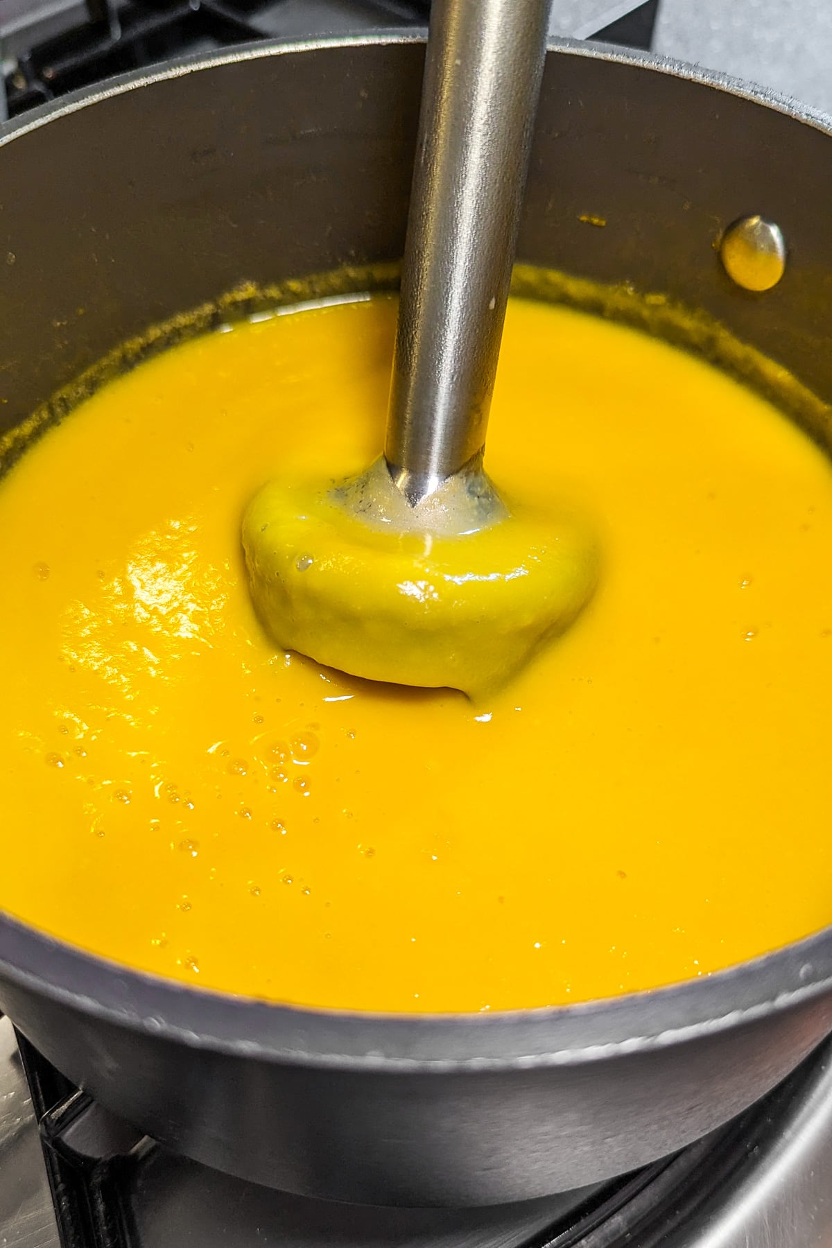 Mixing pumpkin soup with a manual blender in a pan on the stove.