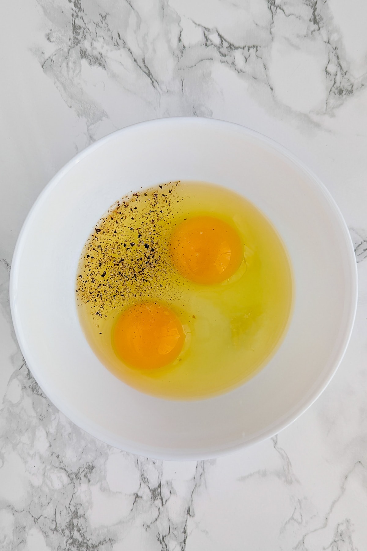 Top view of a white plate with 2 eggs, black pepper and salt.