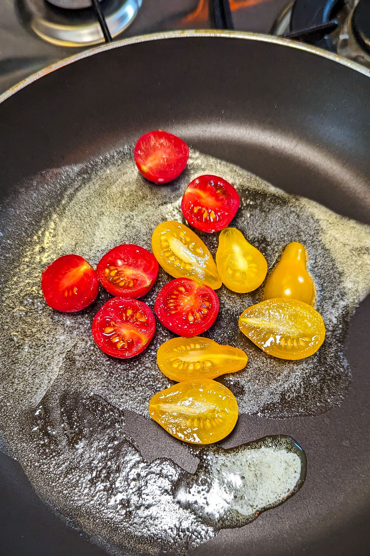 Cooking yellow and red cherry tomatoes in a frying pan in melted butter.