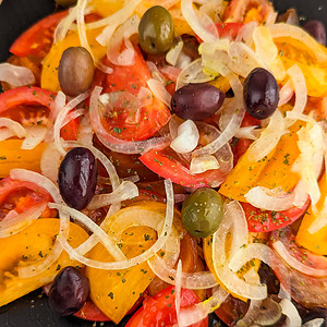 Close view of a black plate with a salad of tomato, onion and olives.