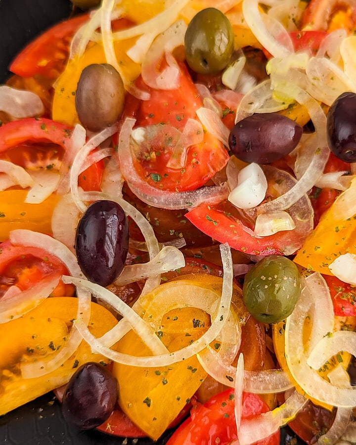 Close view of a black plate with a salad of tomato, onion and olives.