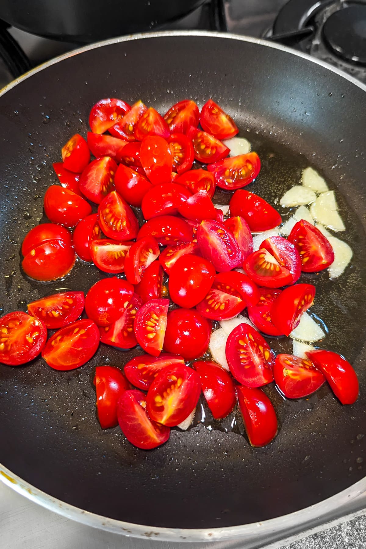 Tomatoes and garlic in a frying pan on the stove.