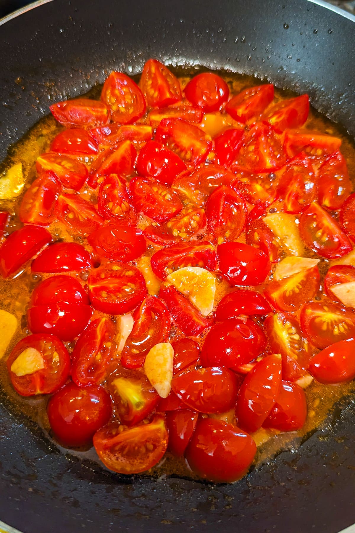 Cooked tomatoes and garlic in a frying pan on the stove.