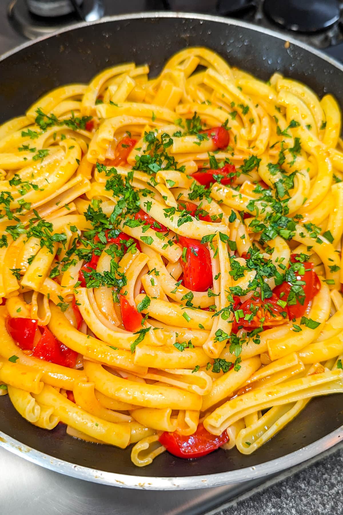 Close look of a pan of pasta with tomatoes, garlic and parsley.