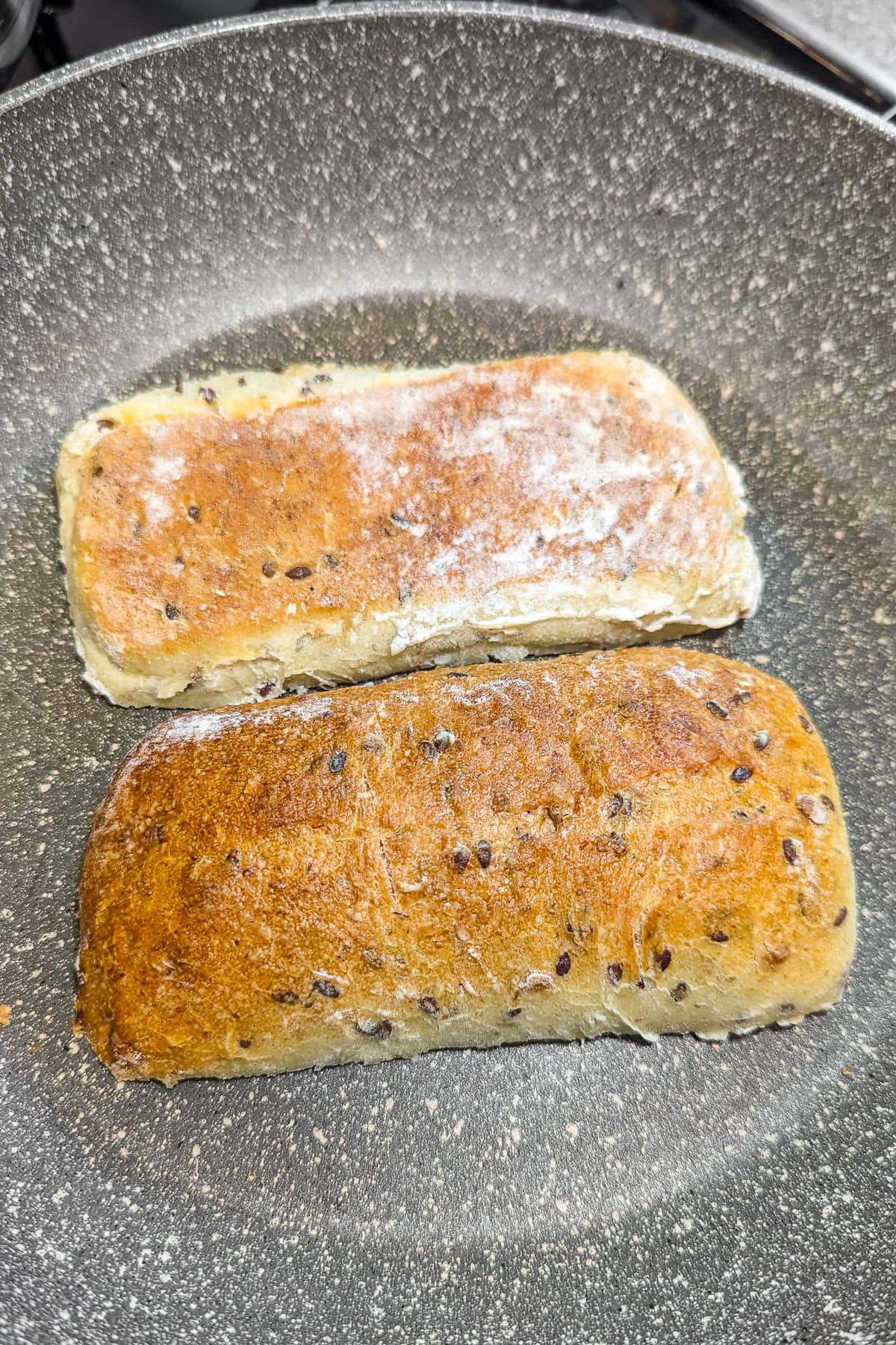 Roasting two halves of chiabatta bread in a frying pan.