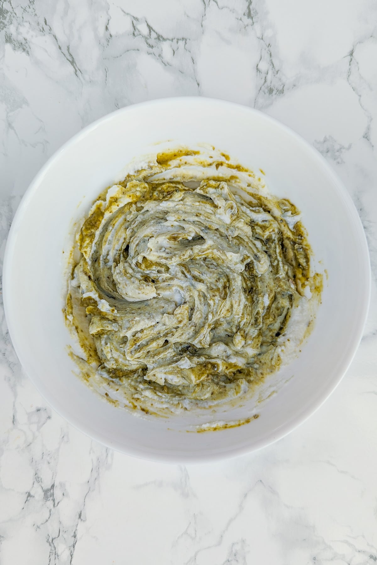 Top view of a white plate with a mix of ricotta and basil pesto on a white marble table.