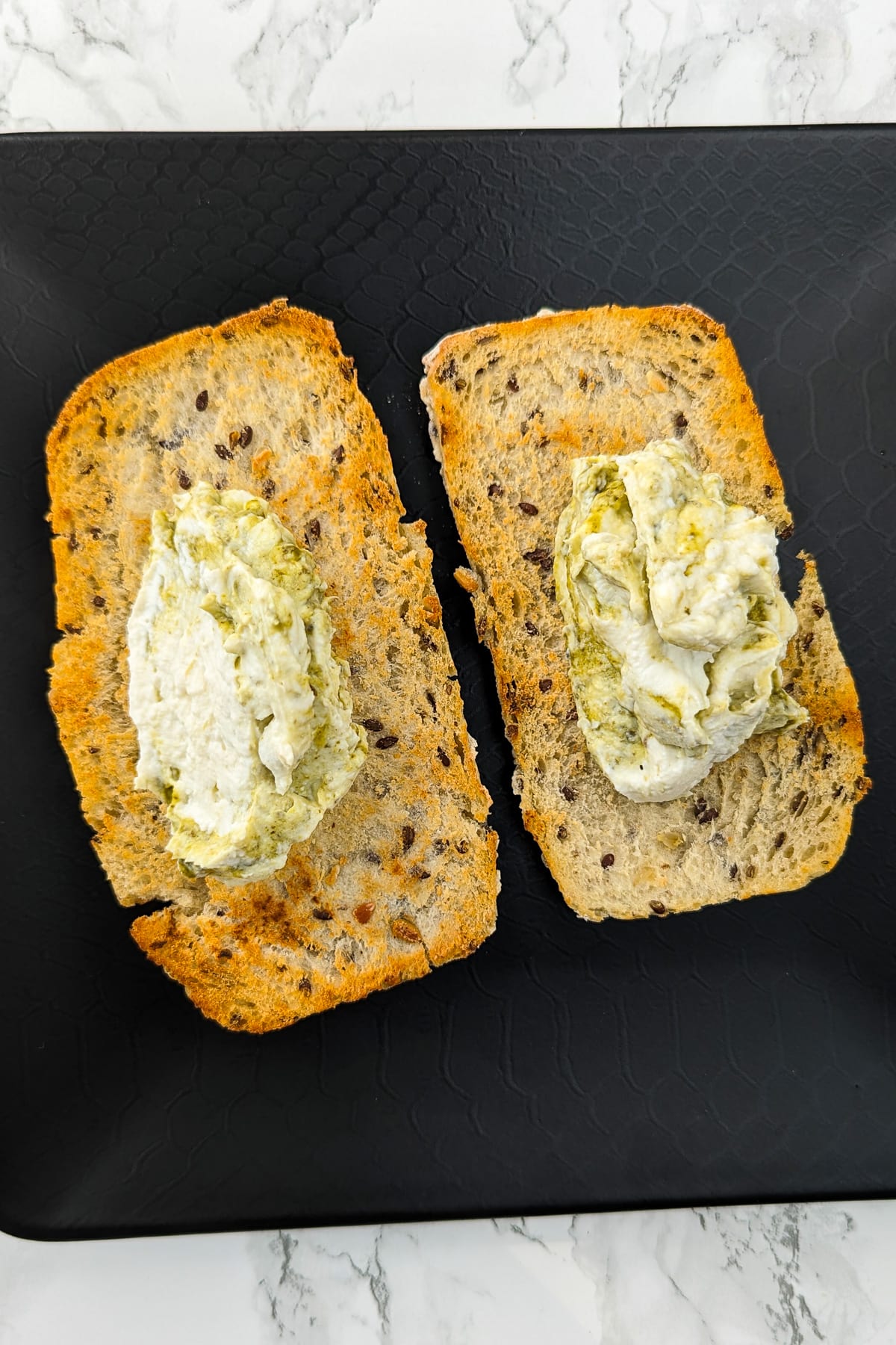 Two slices of bread topped with a mix of cream cheese and basil pesto.