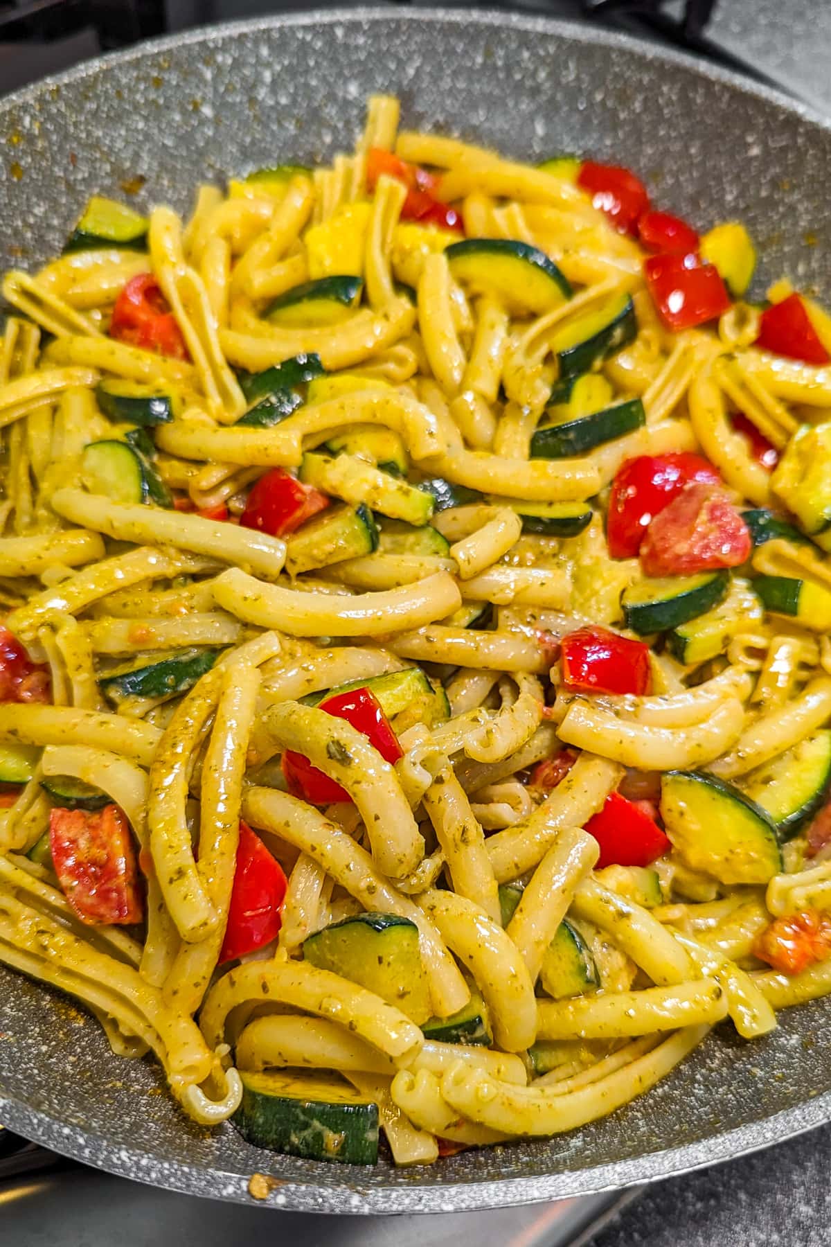 Zucchini and tomato pasta with basil pesto in a frying pan.