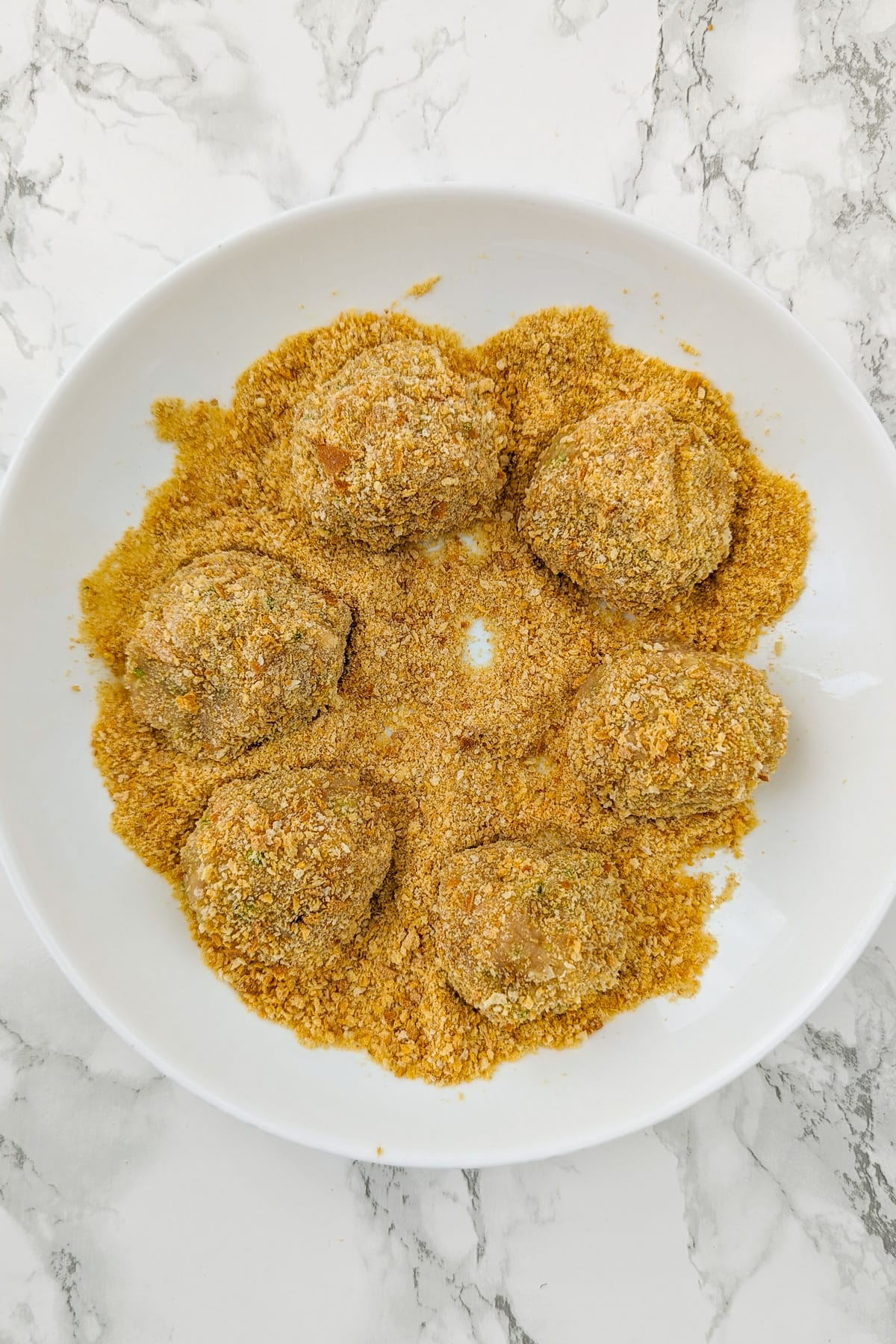 Top view of a white plate with breadcrumbs and meatballs.