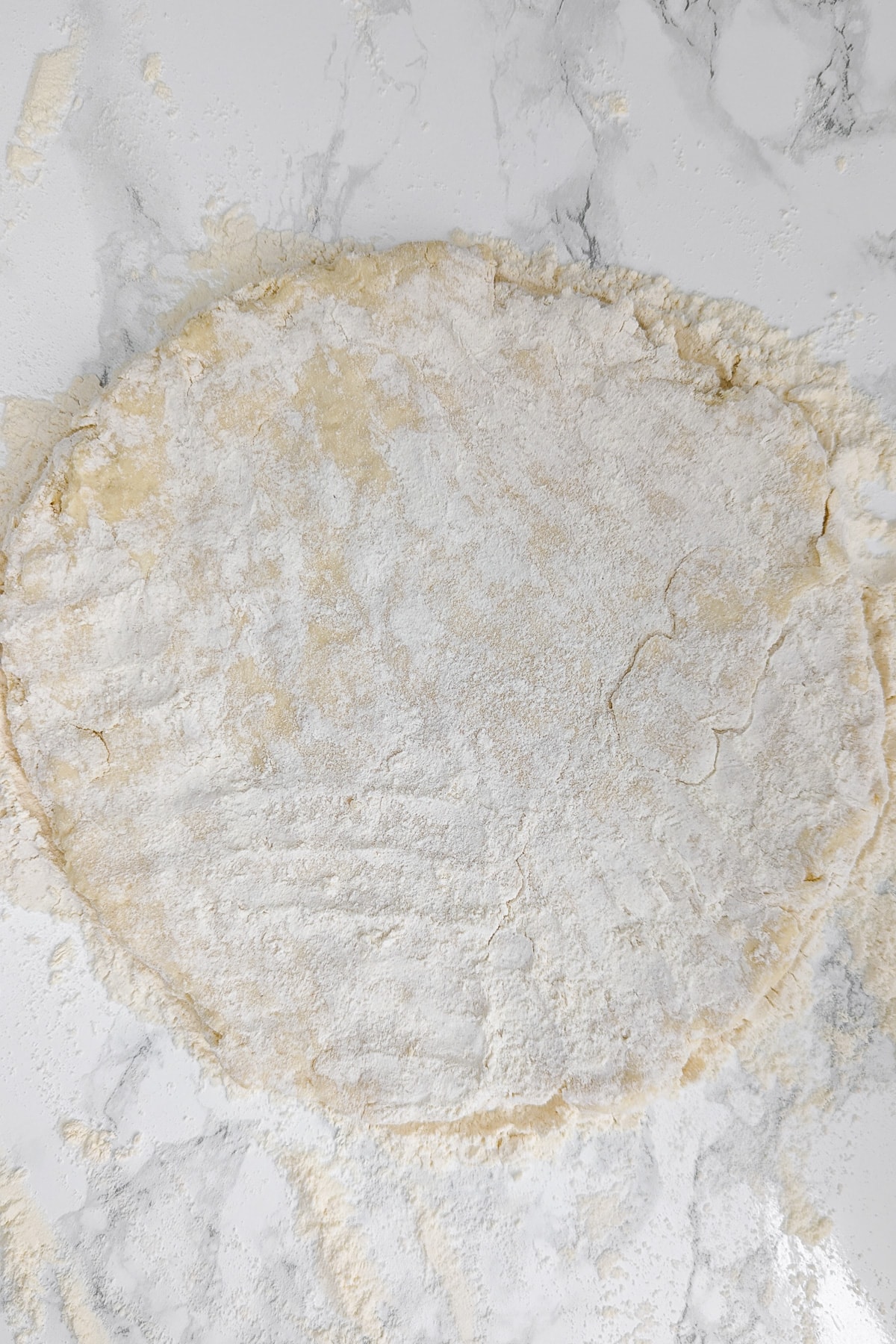 Rounded piece of dough on a white marble table covered with flour.