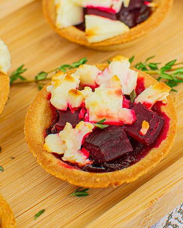 Baked beetroot and feta cheese tartlets near a branch of thyme on a wooden board.