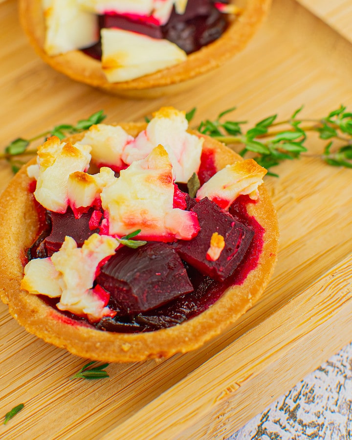 Baked beetroot and feta cheese tartlets near a branch of thyme on a wooden board.