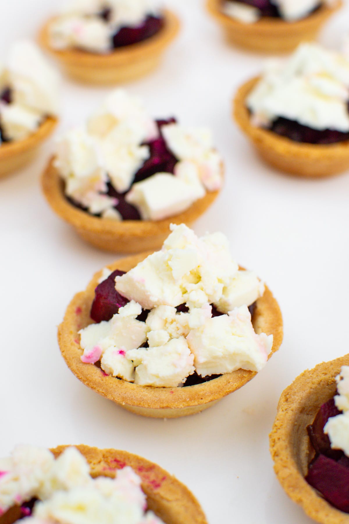 Tartlets with feta cheese, caramelized onions and beetroots on a white traybake.