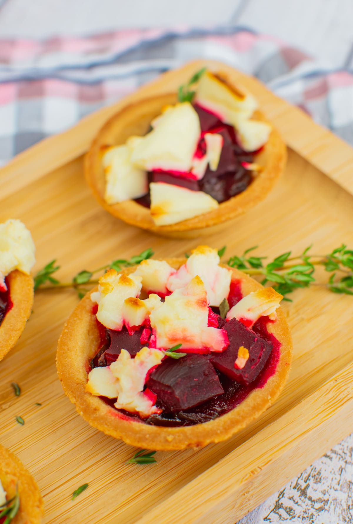 Baked beetroot and feta tartlets with a thyme brunch in the background served on a wooden board.