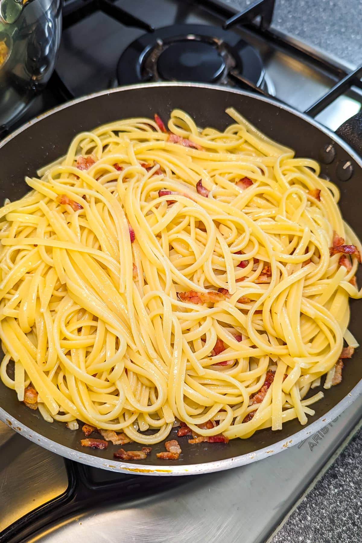 Carbonara sauce pasta in a frying pan on the stove.