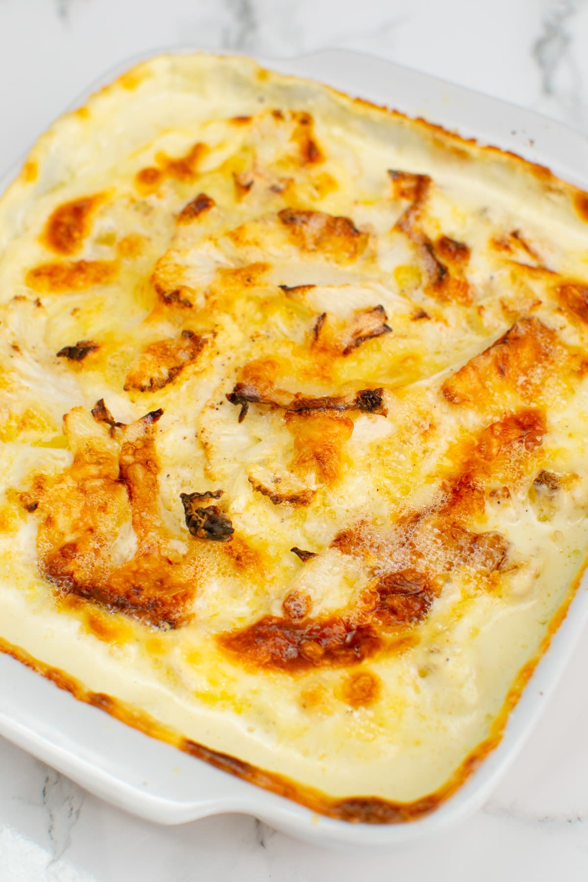 White casserole with cauliflower gratin on a white marble table.