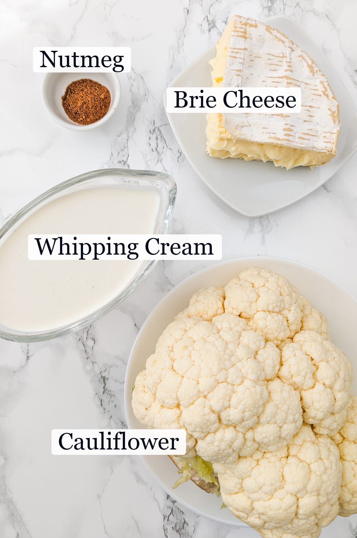 Cauliflower, whipping cream, nutmeg and brie cheese on a white marble table.