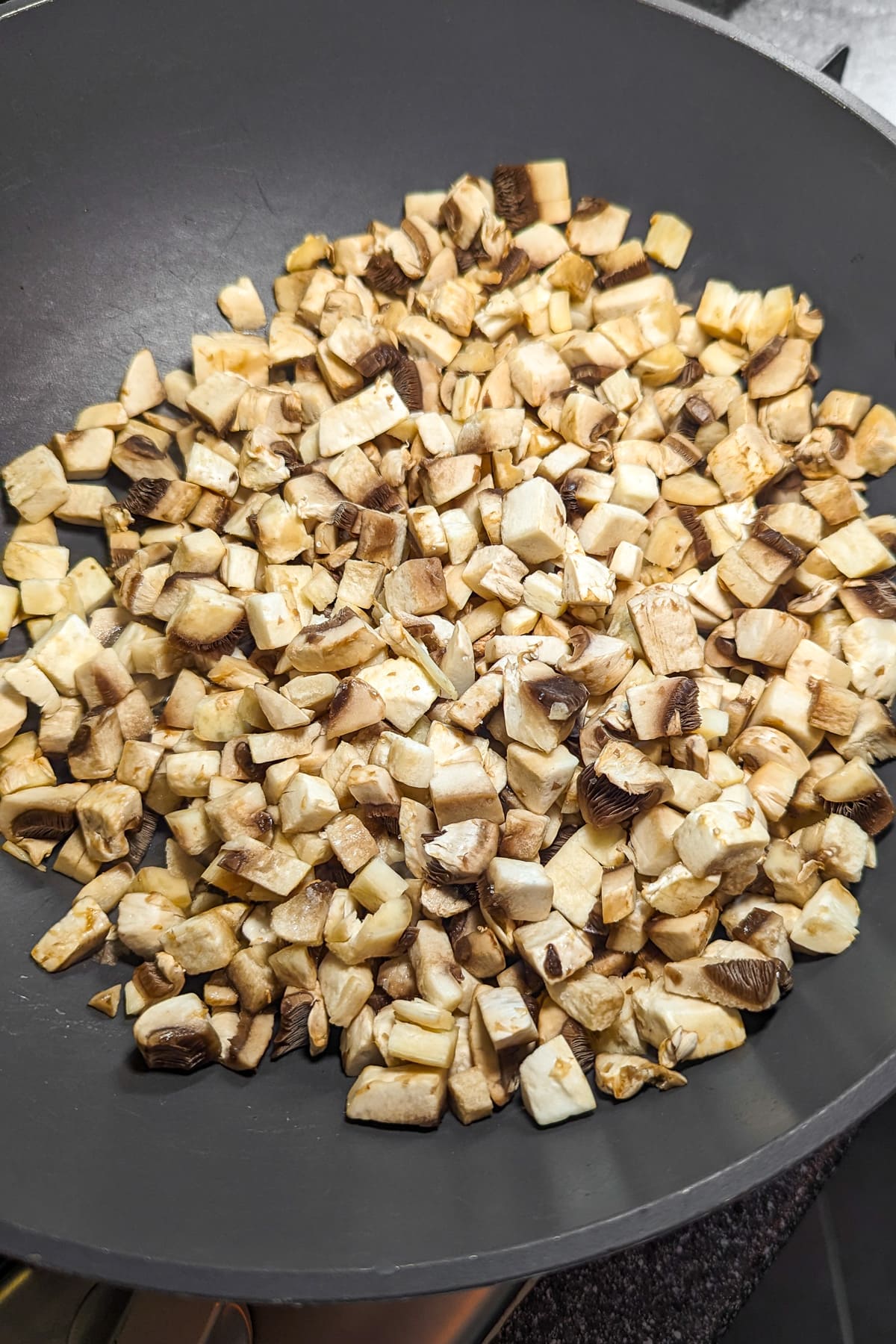 A large wok on the stovetop with small cubes of mushrooms.